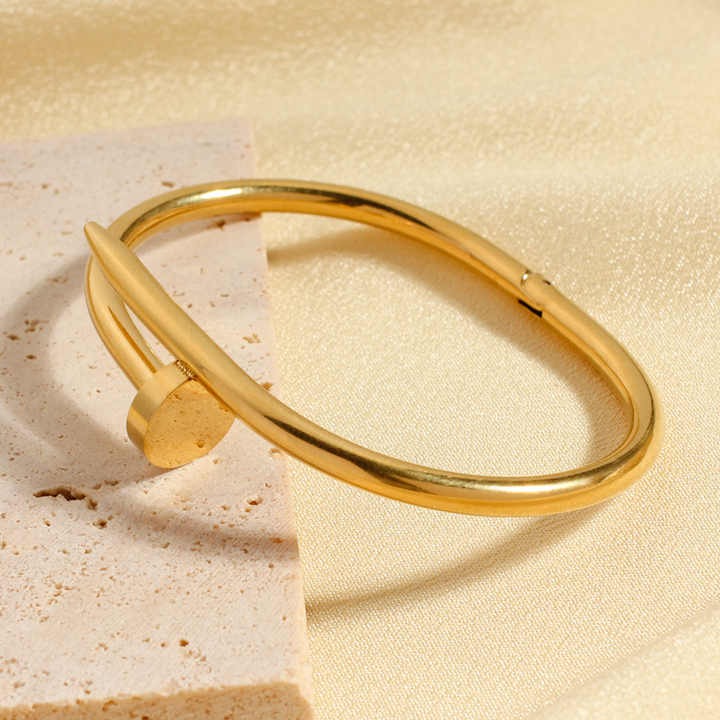 Sleek gold nail bangle styled on marble and fabric backdrop
