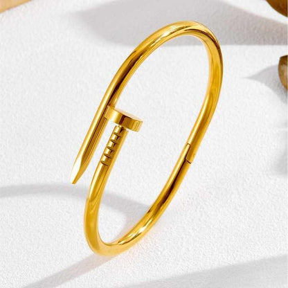 Bold gold nail bracelet standing upright on textured white background