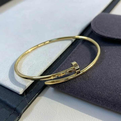 Nail-inspired gold bangle resting on a monochrome leather pouch