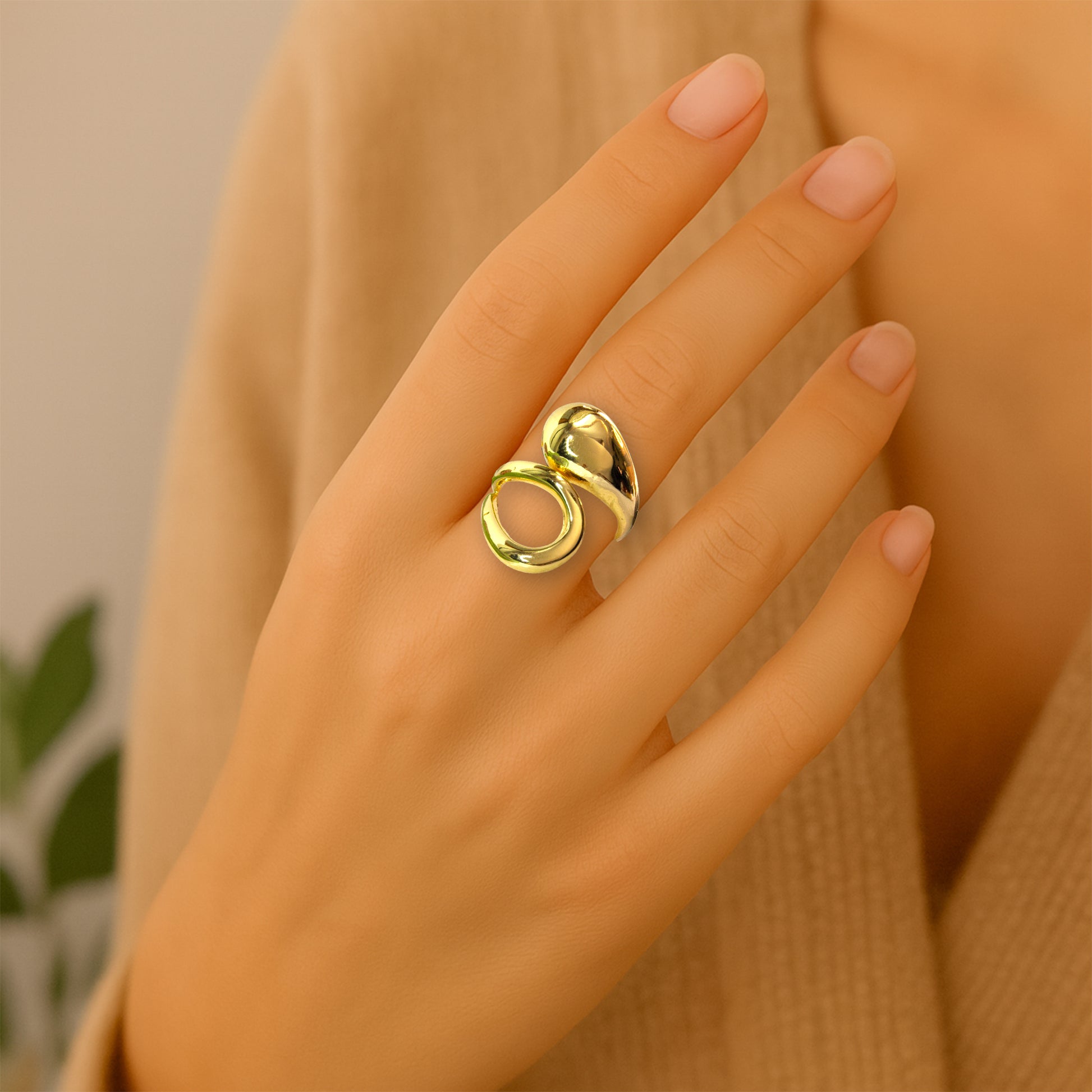 Gold molten drop statement ring worn on woman’s hand, modern lifestyle jewelry shot.