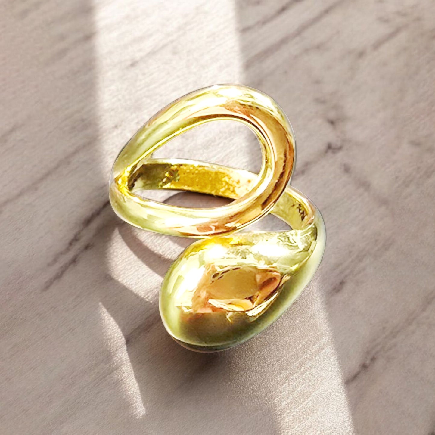 Gold molten drop ring on marble surface with natural sunlight reflection, luxury jewelry flat lay.