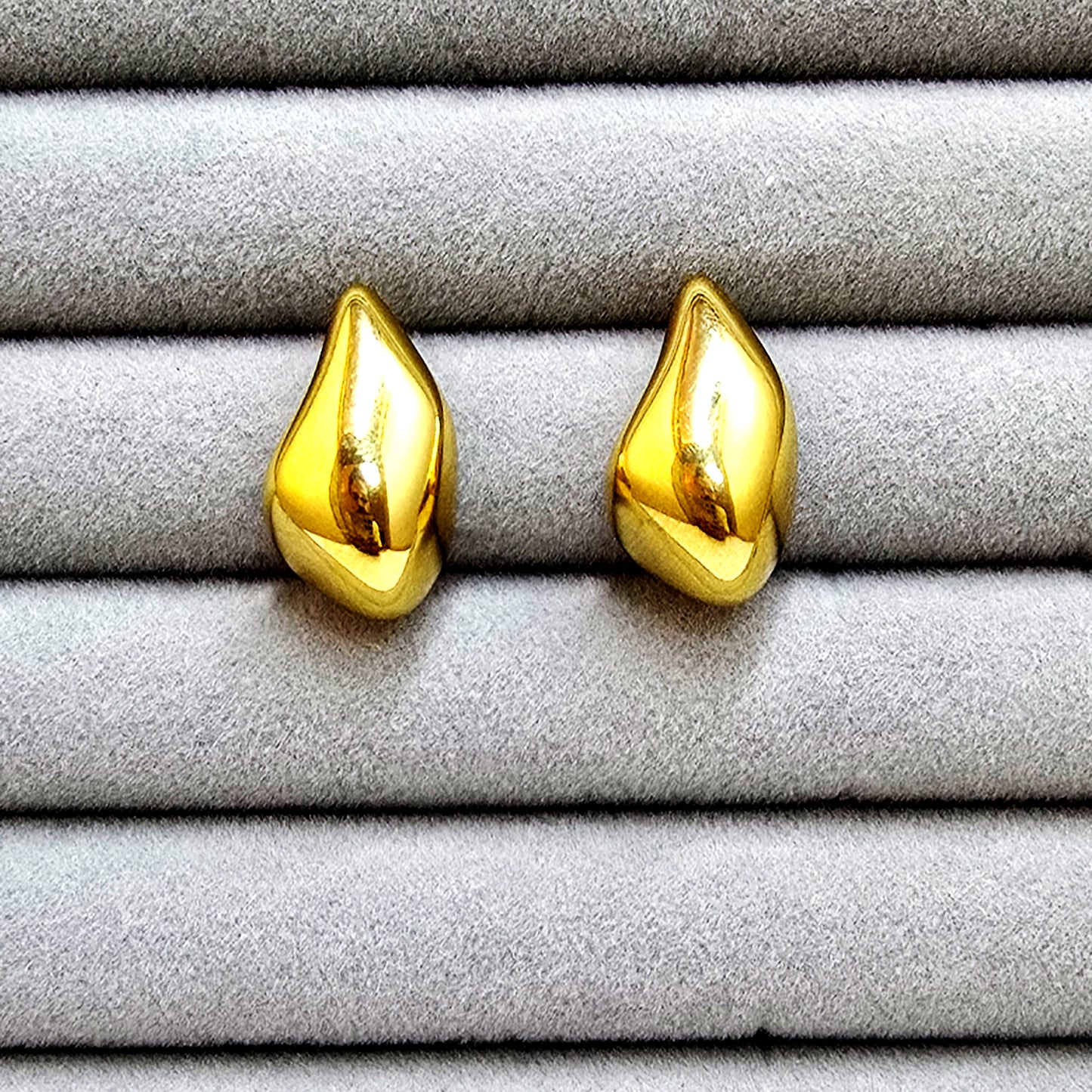 A pair of high-polish gold molten teardrop stud earrings displayed in a grey velvet jewelry tray.