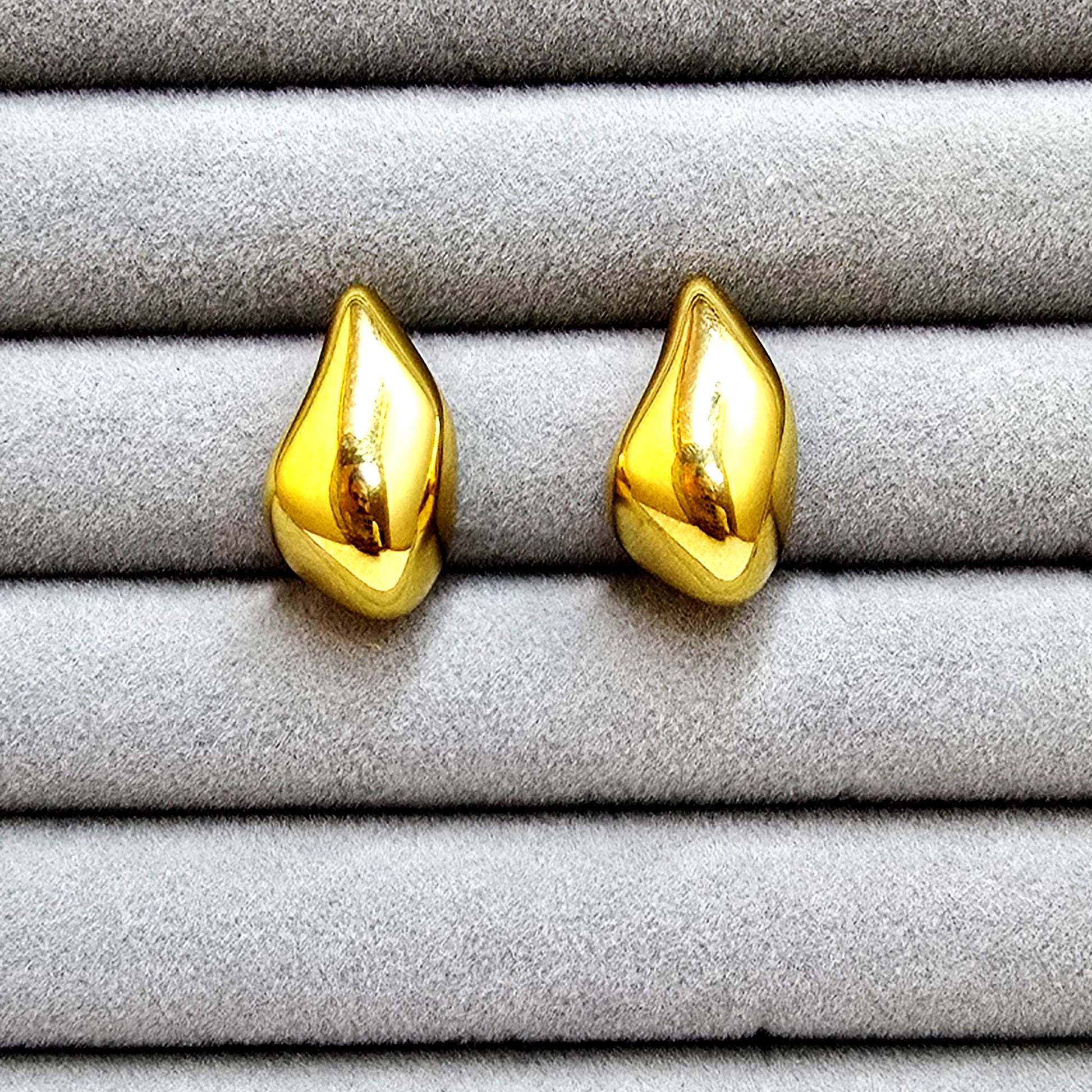 A pair of high-polish gold molten teardrop stud earrings displayed in a grey velvet jewelry tray.