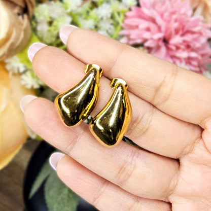 Hand holding a pair of gold molten studs to demonstrate their reflective liquid-metal shine and organic scale.