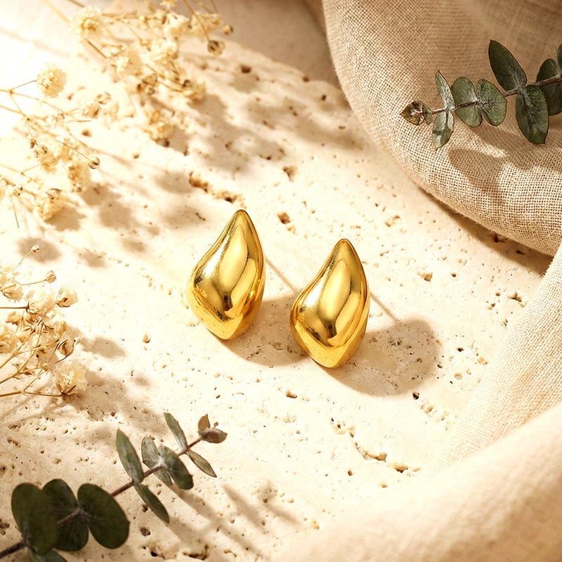 Aesthetic photography of gold molten teardrop earrings on a textured stone surface with dried eucalyptus.