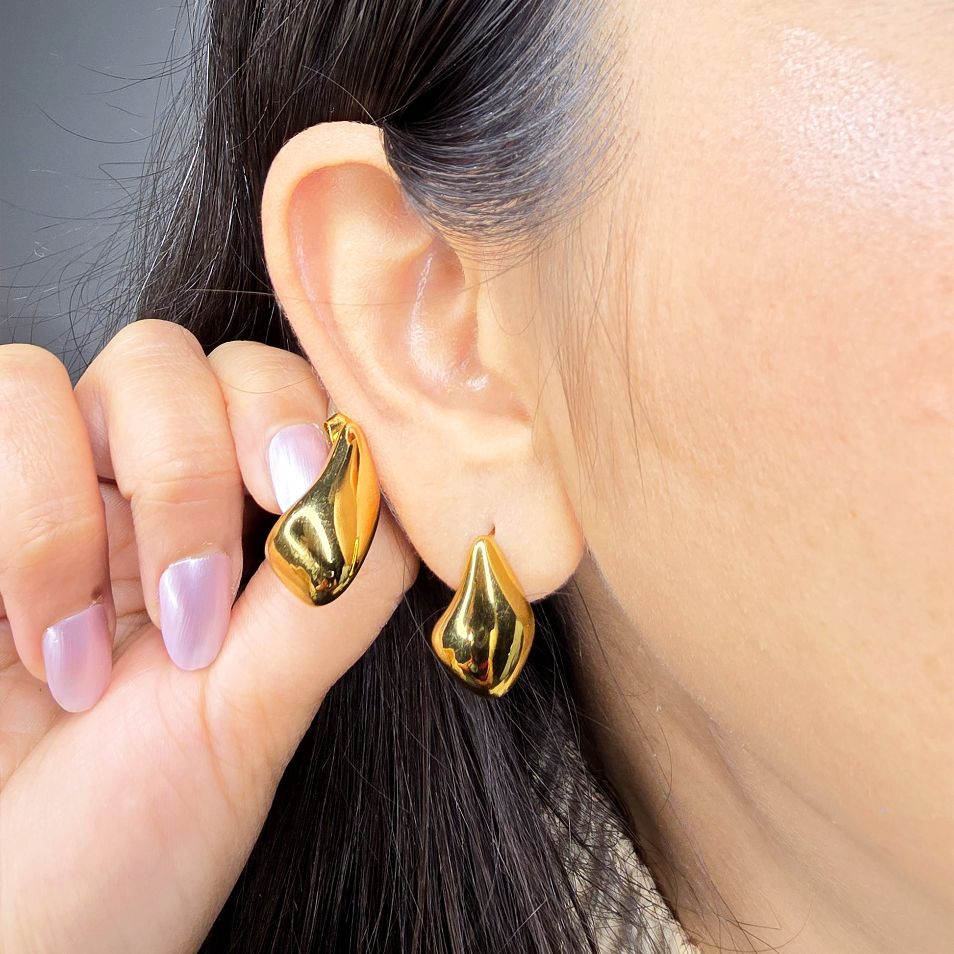 Macro shot of a model wearing a gold molten stud, highlighting the bold liquid-metal silhouette against the skin.
