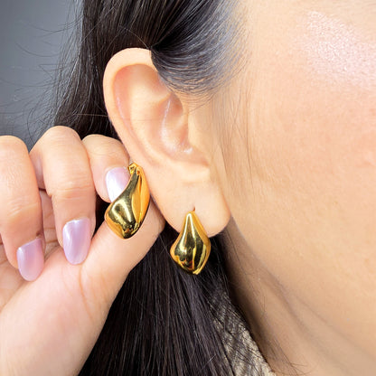 Macro shot of a model wearing a gold molten stud, highlighting the bold liquid-metal silhouette against the skin.