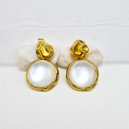 A pair of gold-plated Moon Drop earrings with hammered organic studs and white iridescent circular drops on white rocks.