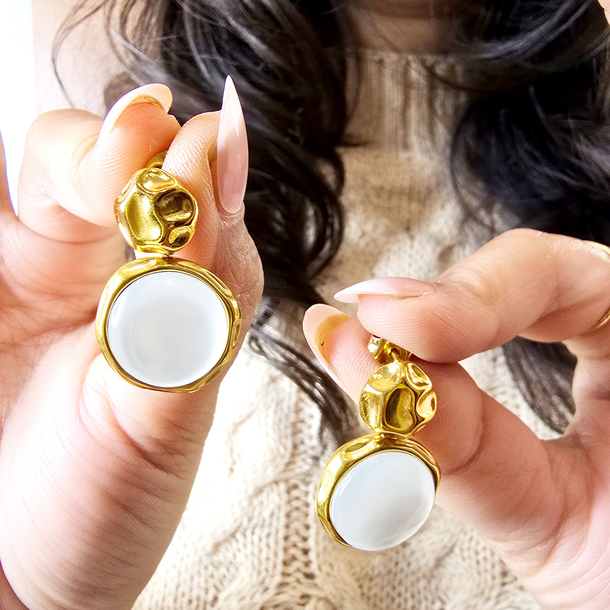 Hand holding a pair of large gold moon drop earrings to show the reflective shine of the hammered metal and the scale of the drops.