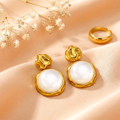 Aesthetic flat lay of moon drop earrings on a peach silk cloth next to a gold ring and dried white flowers.