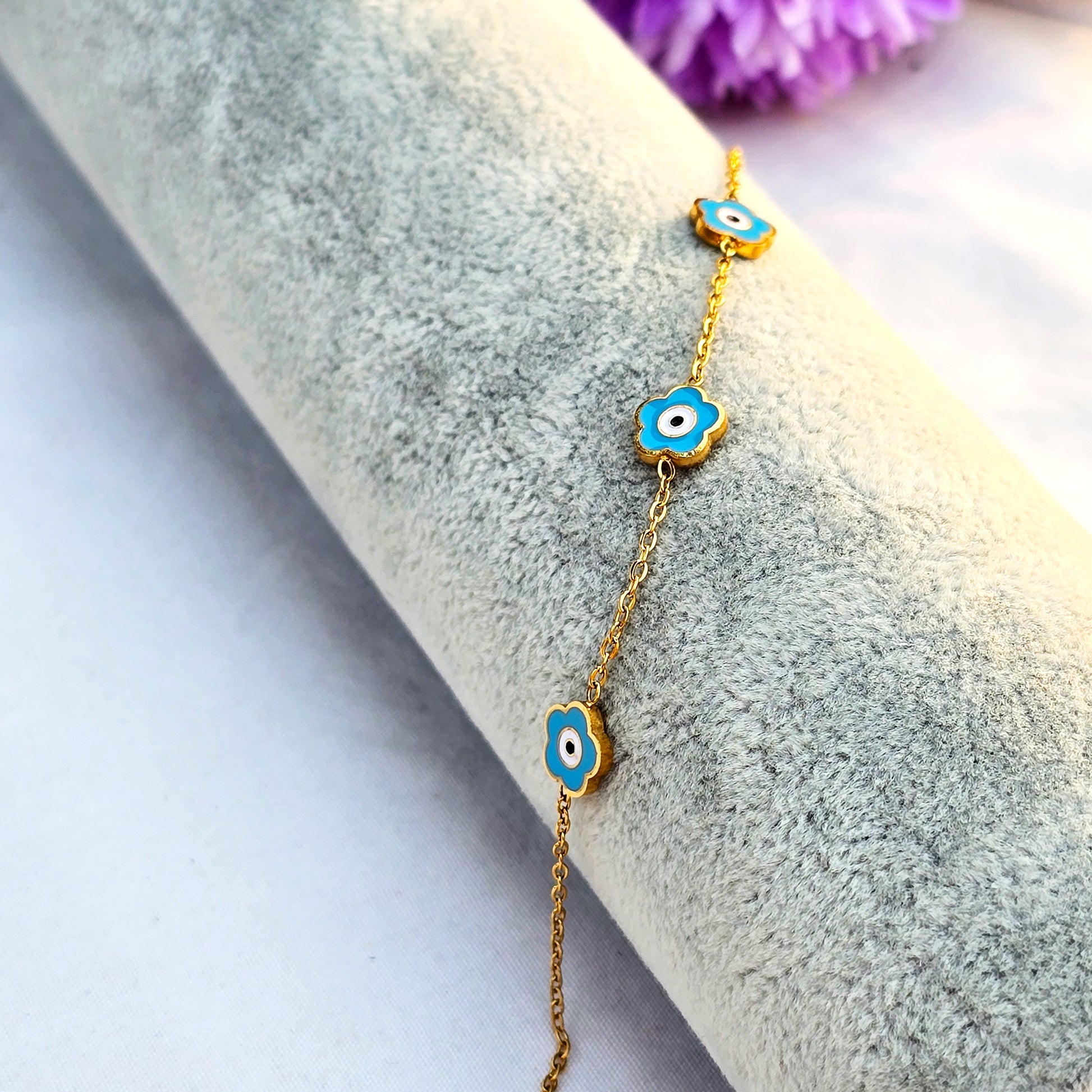 Studio shot of a gold chain bracelet featuring a rectangular bar with teal enamel and a starburst center.