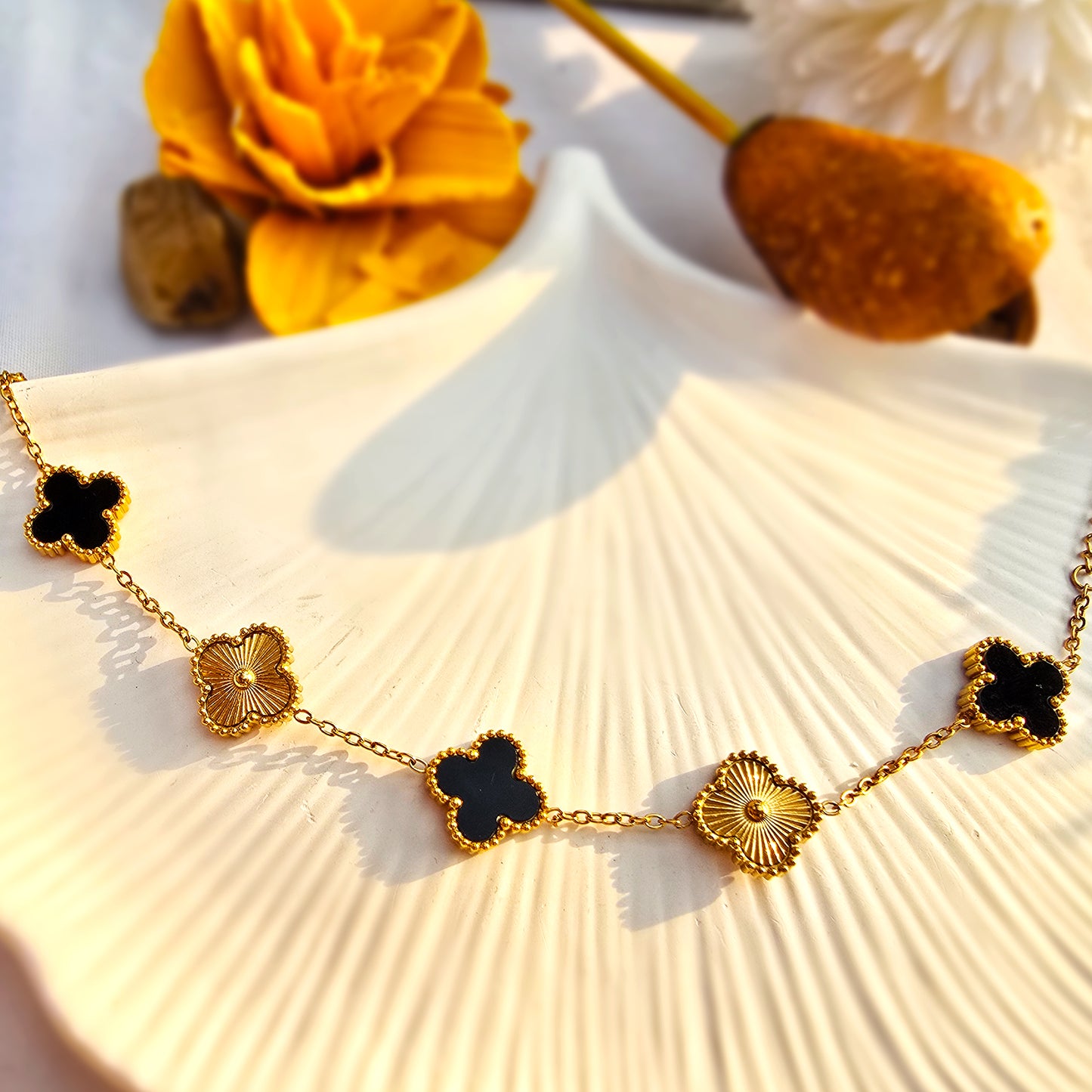 Flat lay of gold chain bracelet with alternating black enamel and textured gold clover charms.