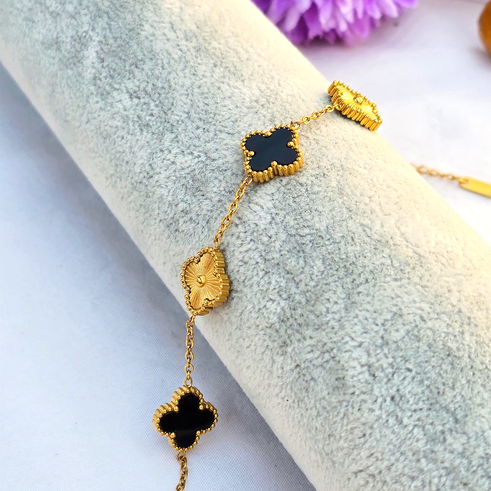 Close-up detail of "guilloché" texture on gold clover charms and black onyx motifs.