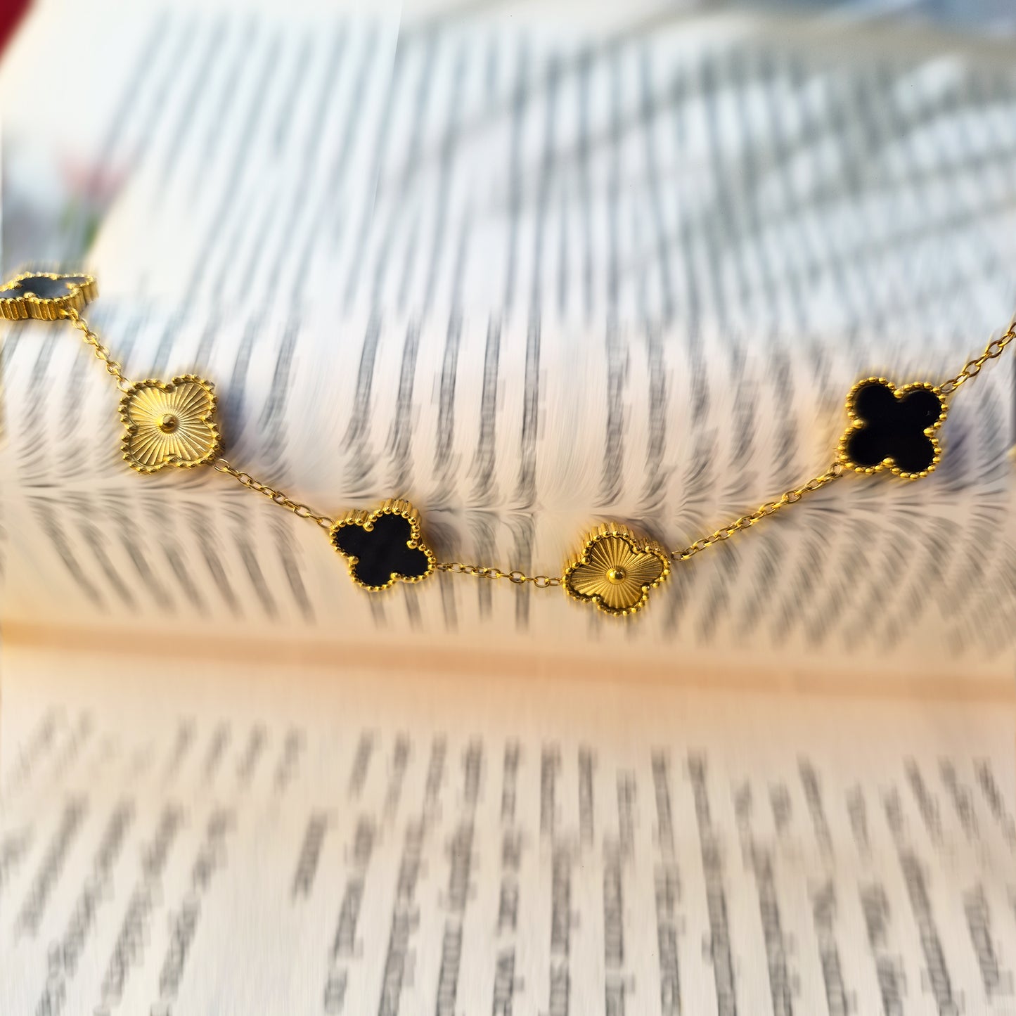 Artistic shot of black and gold clover bracelet draped over open book pages.