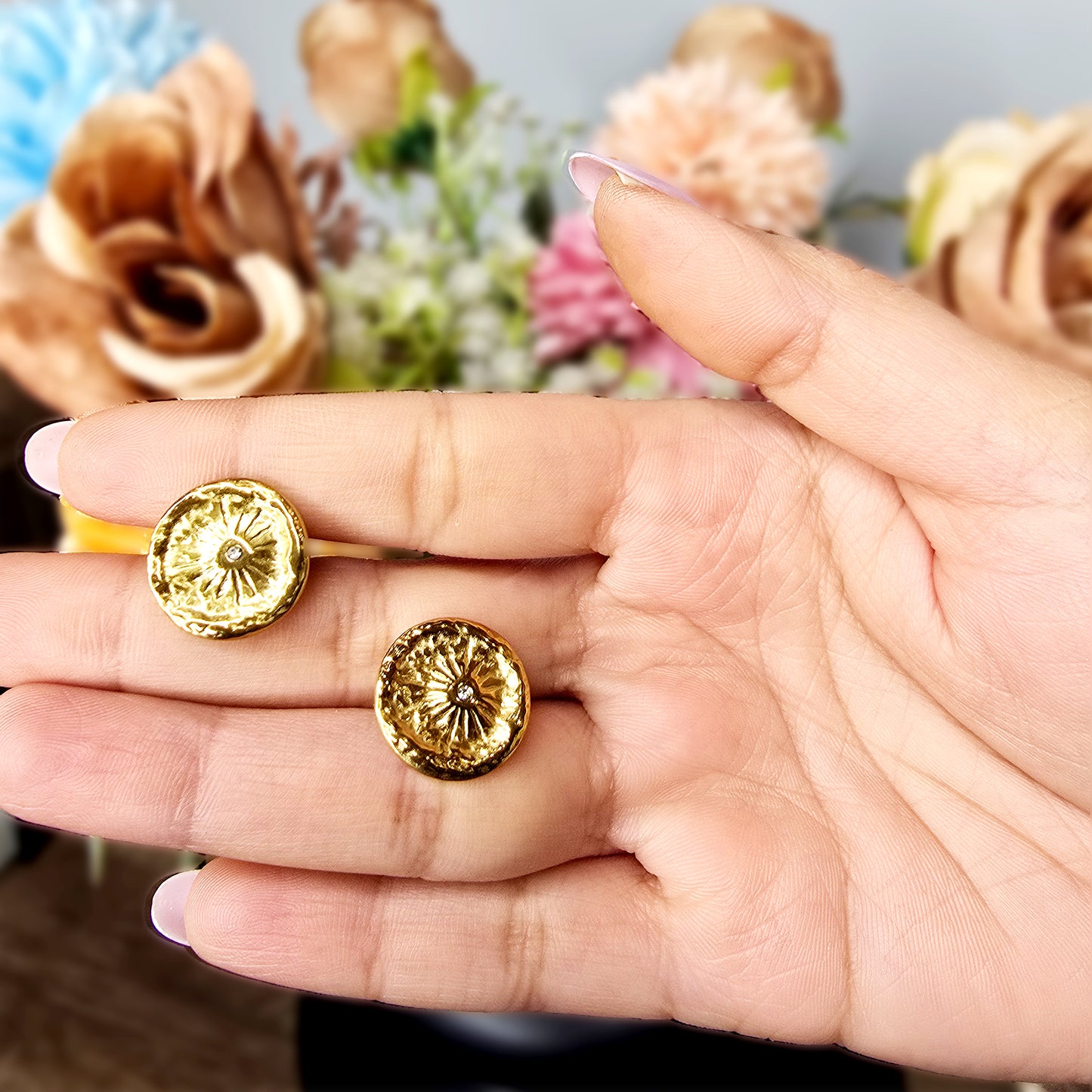 Hand holding two gold Nova Coin earrings to show the reflective hammered texture and delicate starburst engraving.