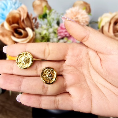 Hand holding two gold Nova Coin earrings to show the reflective hammered texture and delicate starburst engraving.