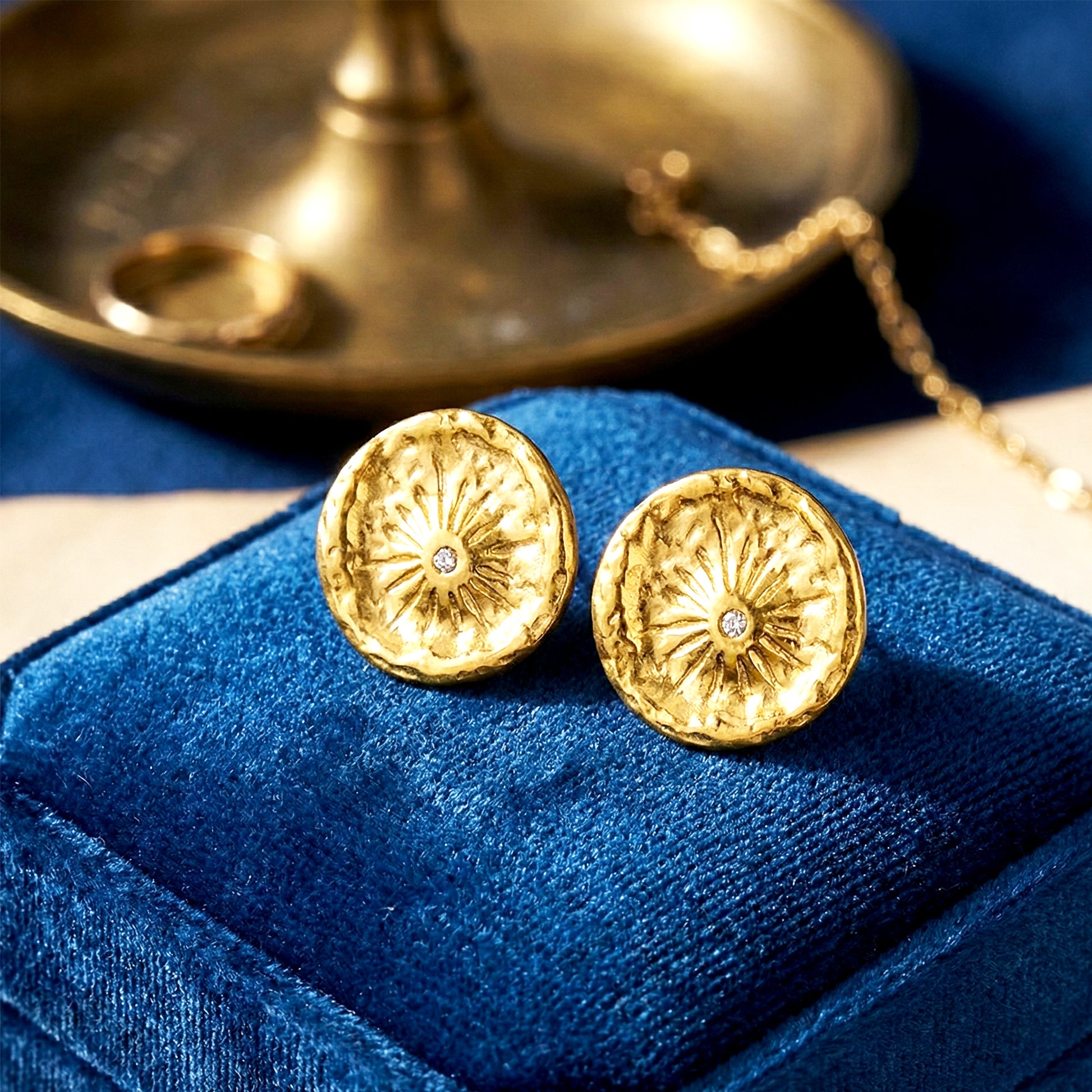Aesthetic photography of gold coin earrings nestled in a blue velvet jewelry box under soft light.