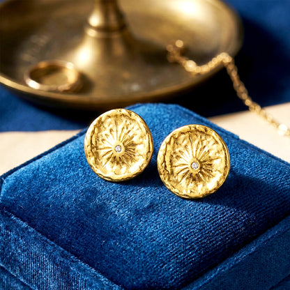 Aesthetic photography of gold coin earrings nestled in a blue velvet jewelry box under soft light.