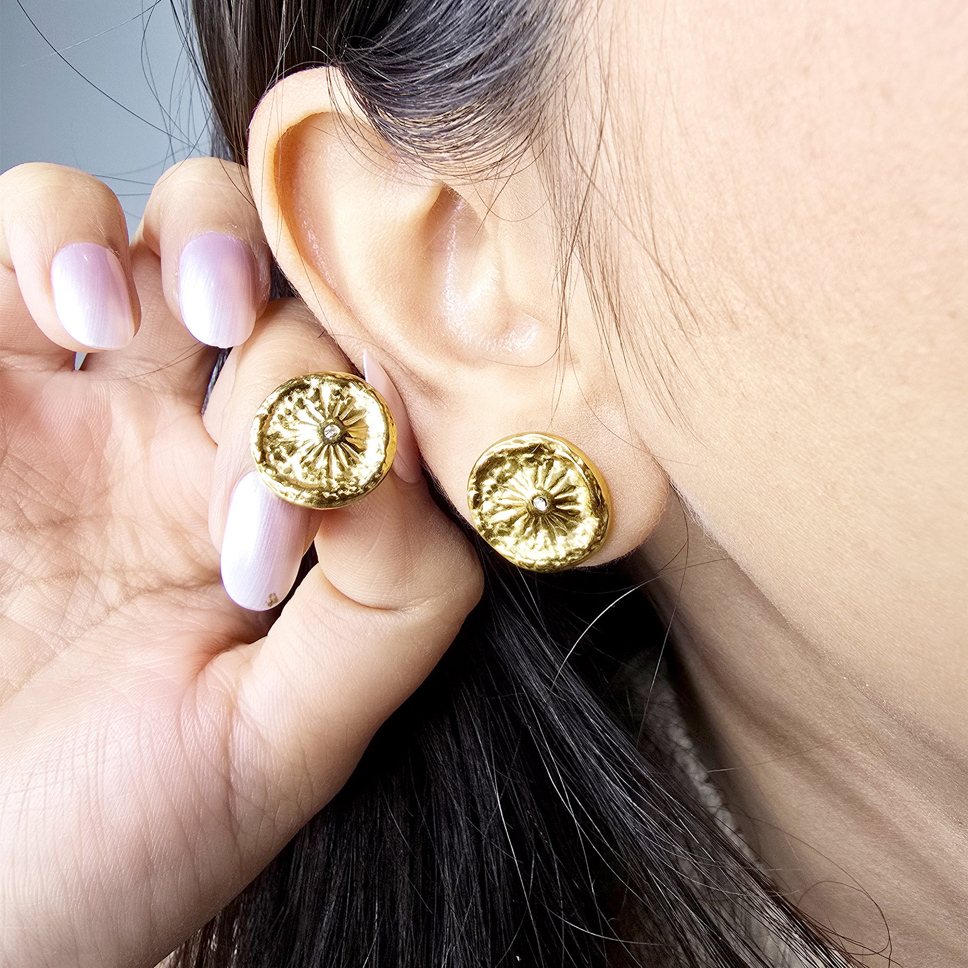 Macro shot of a model wearing the gold Nova Coin earring, highlighting the sunburst design against the earlobe.