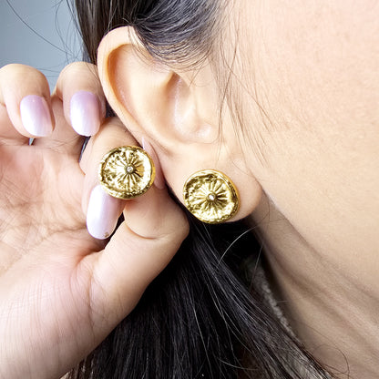 Macro shot of a model wearing the gold Nova Coin earring, highlighting the sunburst design against the earlobe.