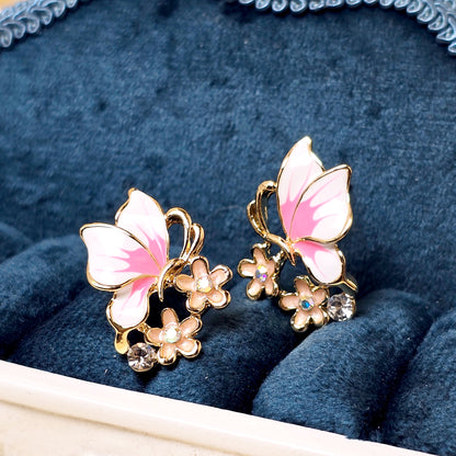 Butterfly-shaped earrings with pink wings and gold accents on a blue velvet background