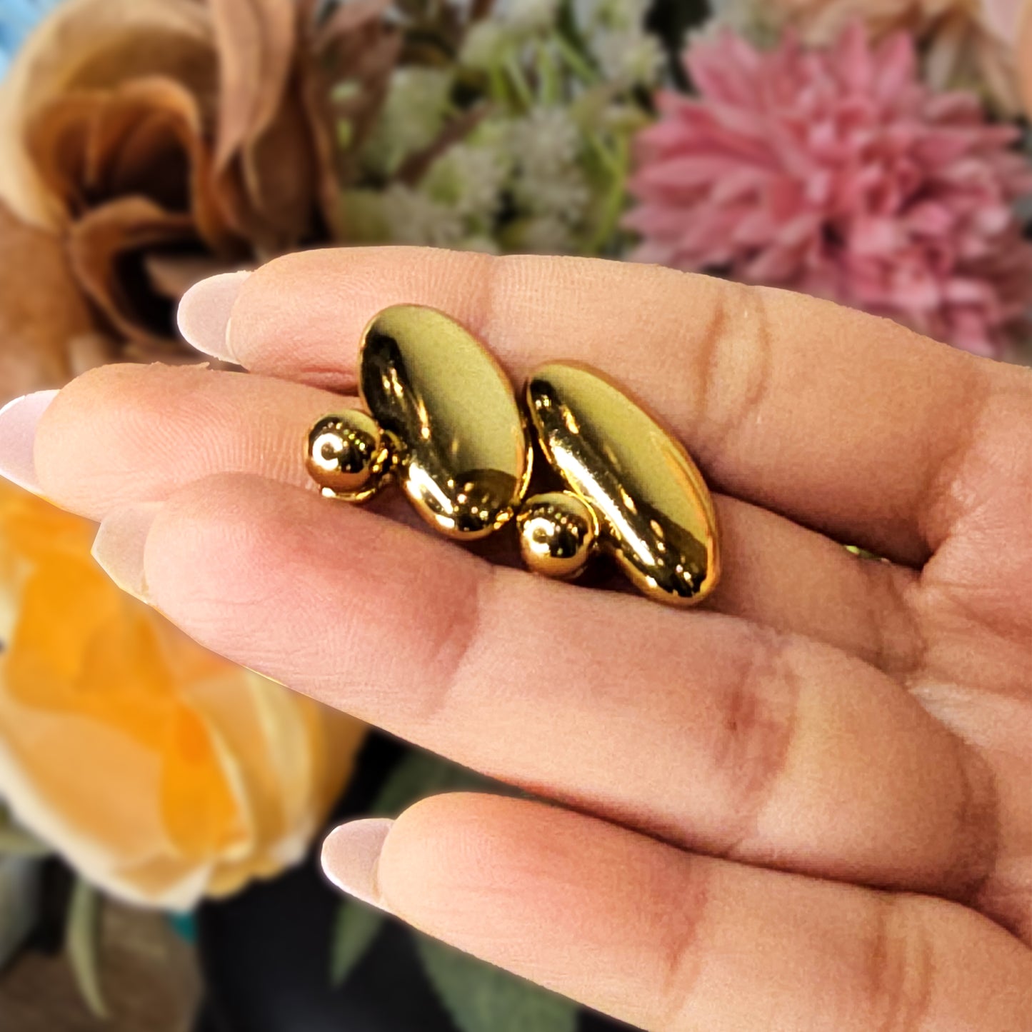 Hand holding two large gold pebble earrings to show the reflective liquid-gold finish and unique organic shape.