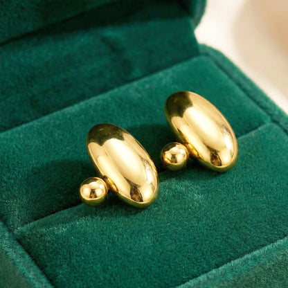 Aesthetic photography of gold pebble studs nestled in a green velvet jewelry box under warm lighting.