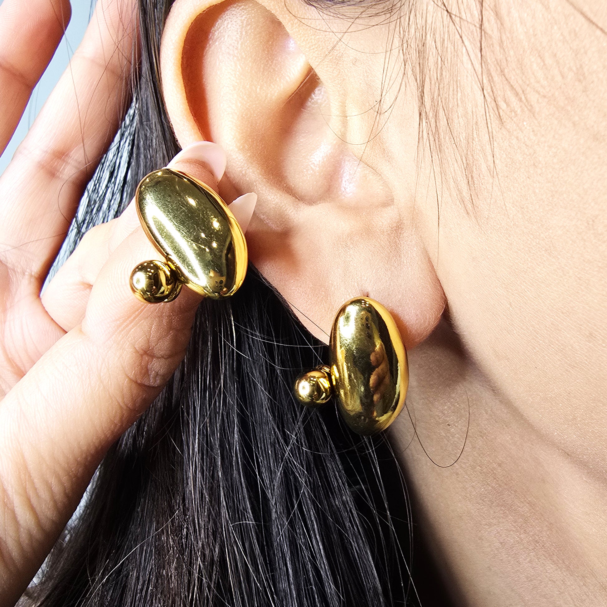Side profile macro shot of a model wearing the gold pebble earrings, highlighting the bold sculptural silhouette.