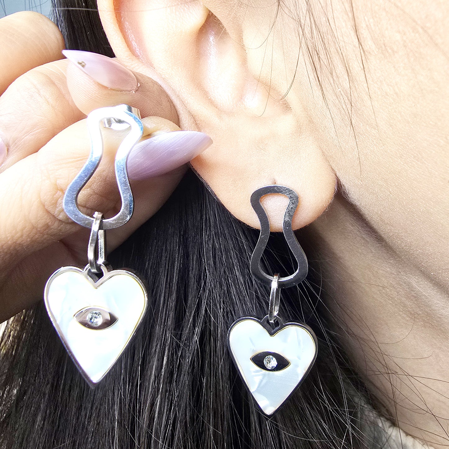 Macro shot of a model wearing silver Prism Eye dangles, highlighting the geometric link and crystal-centered heart.