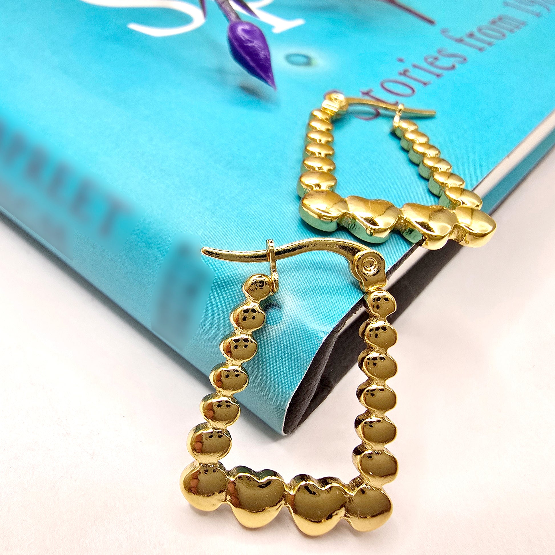 Rectangle Heart Hoop Earrings – chic gold hoops placed on a blue book