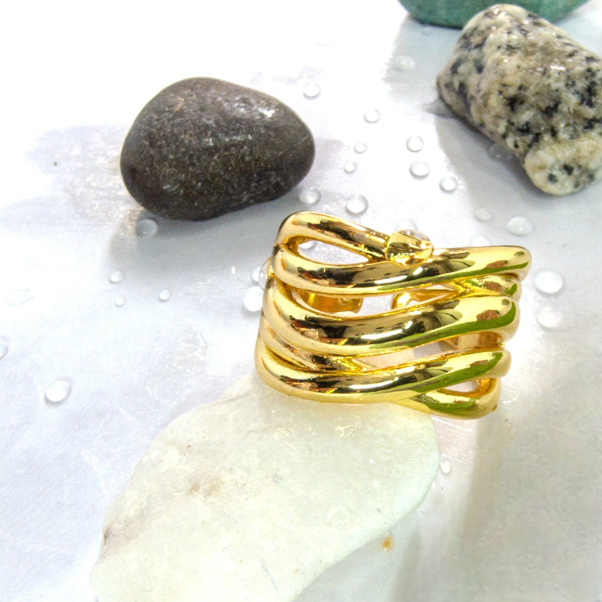A gold Ripple Band Ring placed on white stone with water droplets, showcasing its layered wave design.