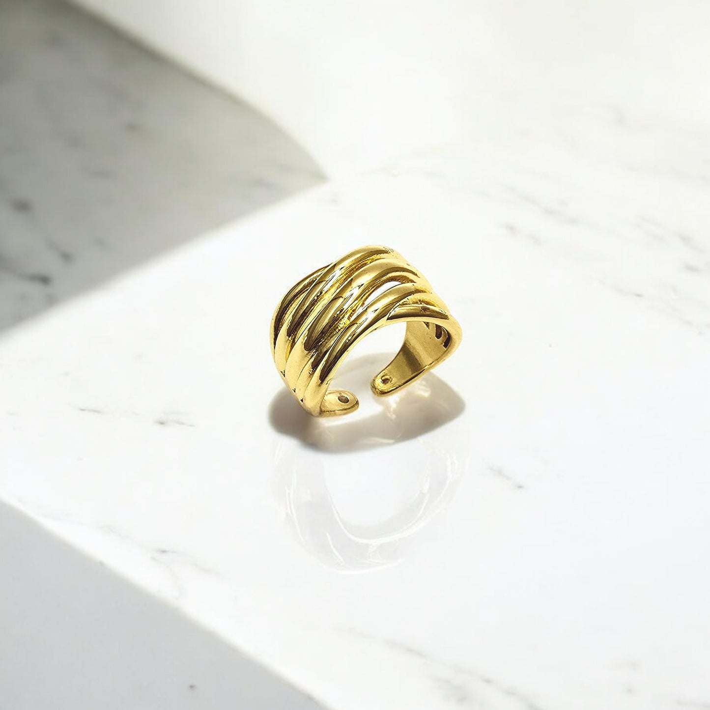 Ripple Band Ring on marble background, highlighting its gold shine and adjustable open band.