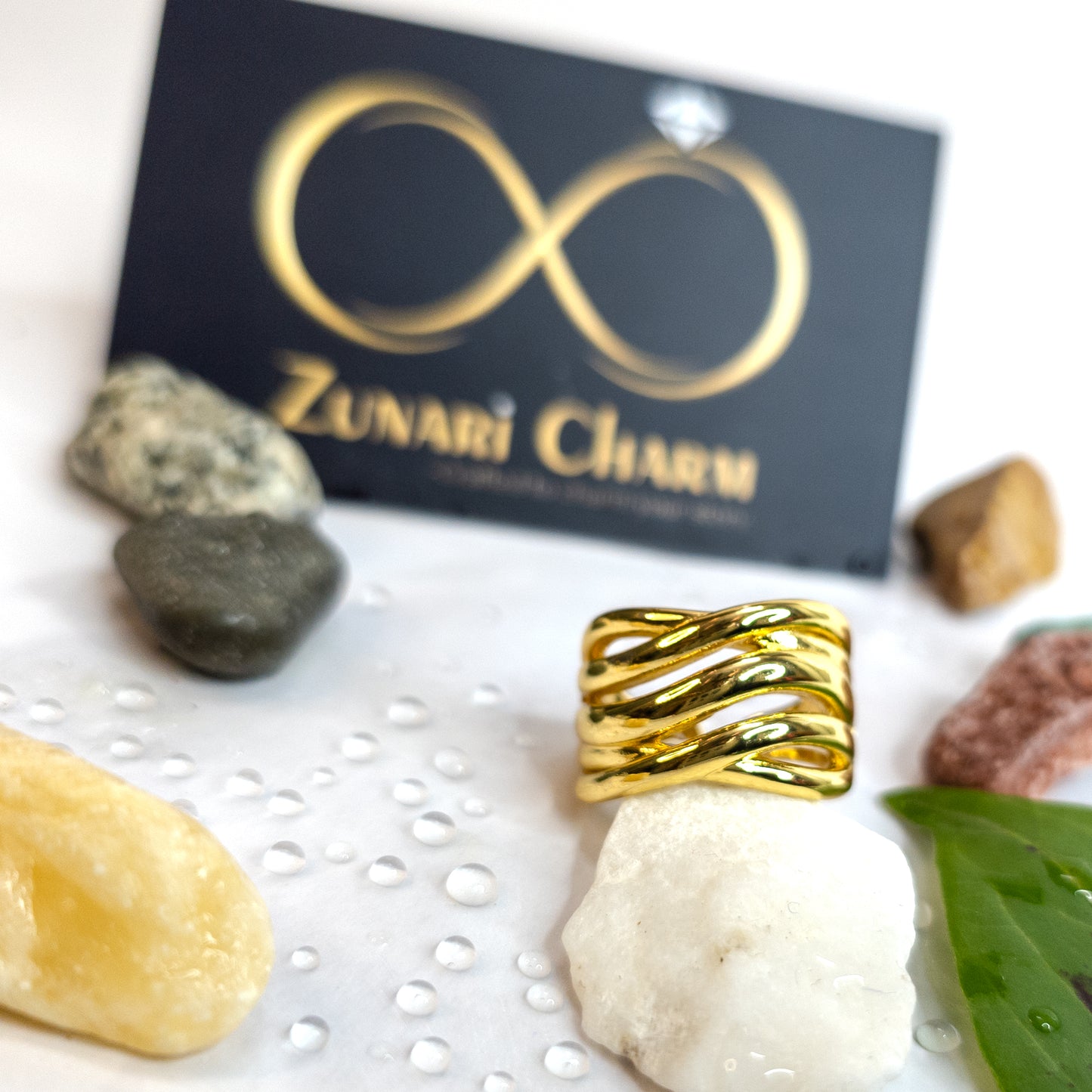Ripple Band Ring displayed with Zunari Charm branding, surrounded by natural stones and droplets.