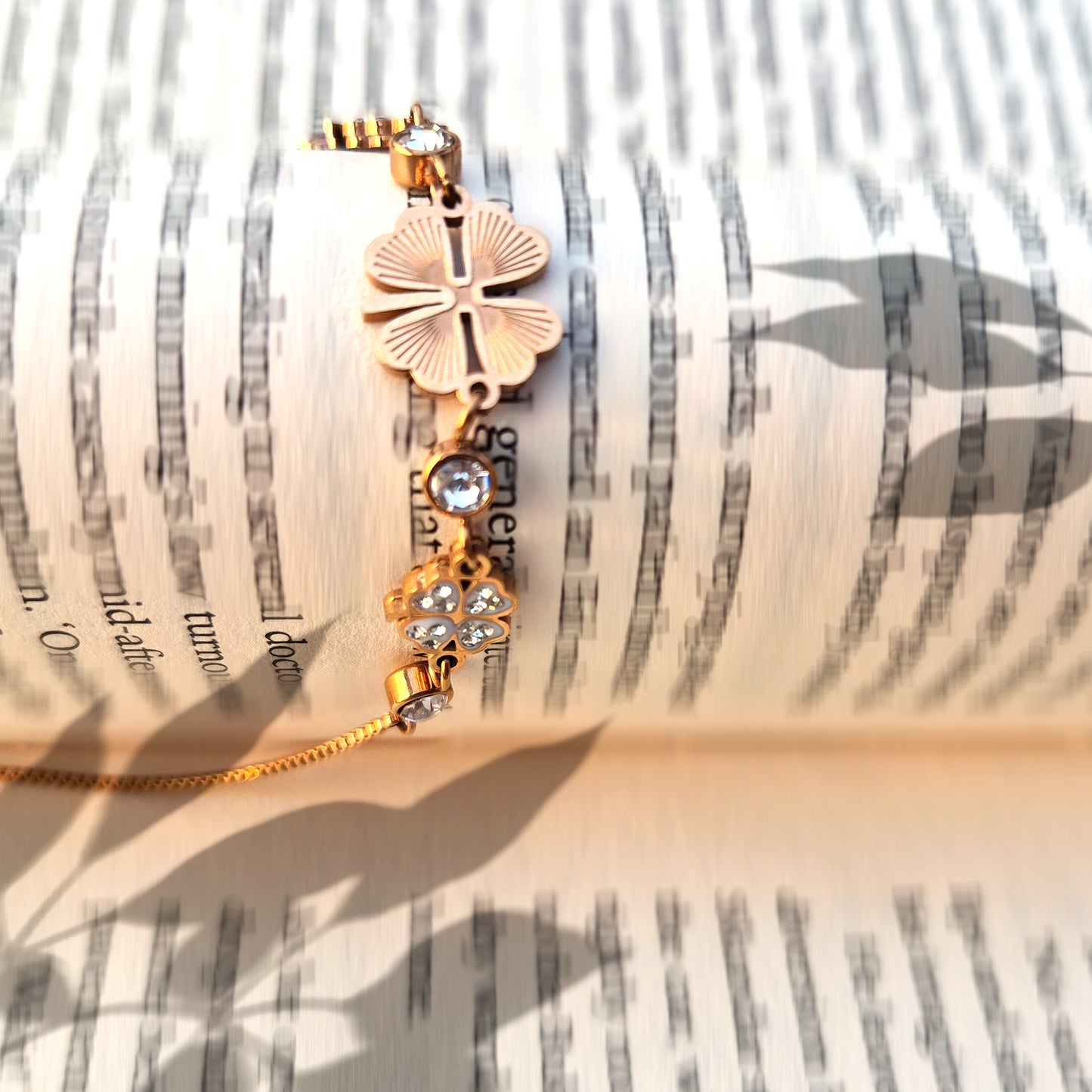 Gold chain bracelet with a black four-leaf clover charm resting on an open book.
