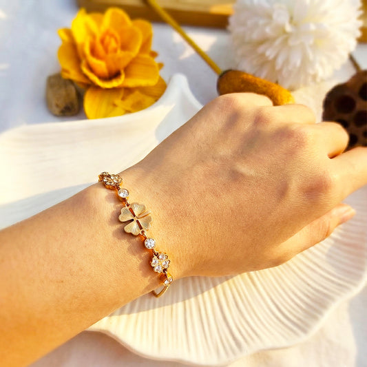 Woman’s wrist wearing a delicate gold bracelet with a black clover motif.