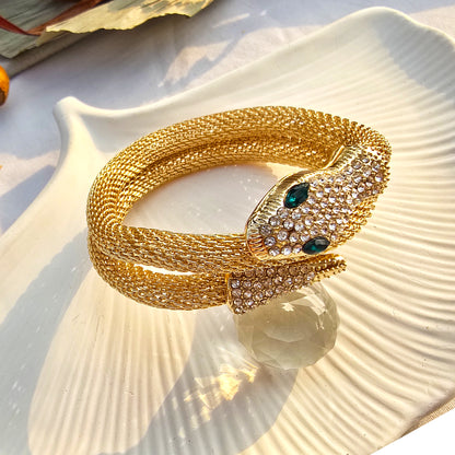 Side view of woven mesh gold snake bracelet highlighting flexible texture and green eyes.