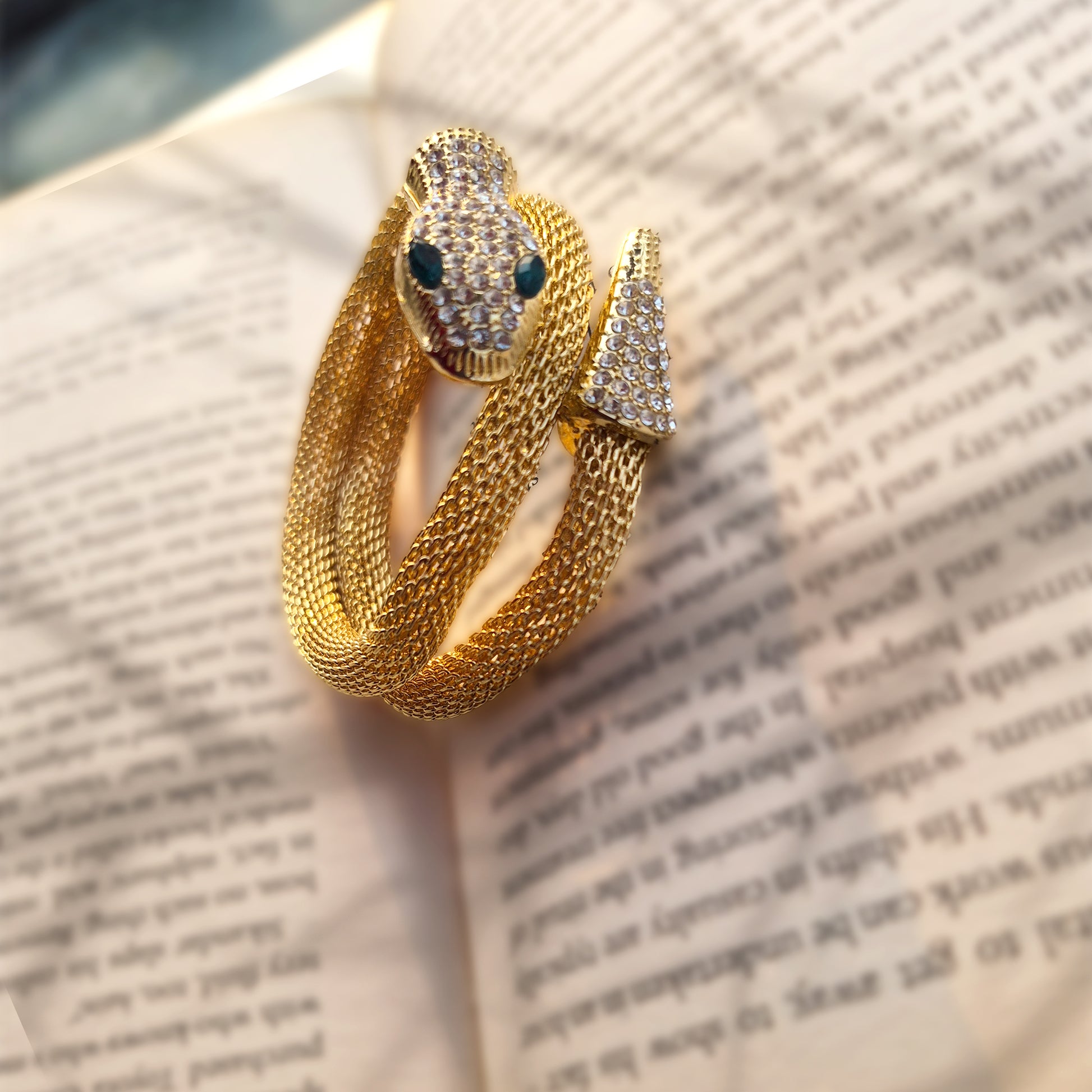 Flexible gold mesh snake bracelet with crystal pave head and emerald green eyes on book page.