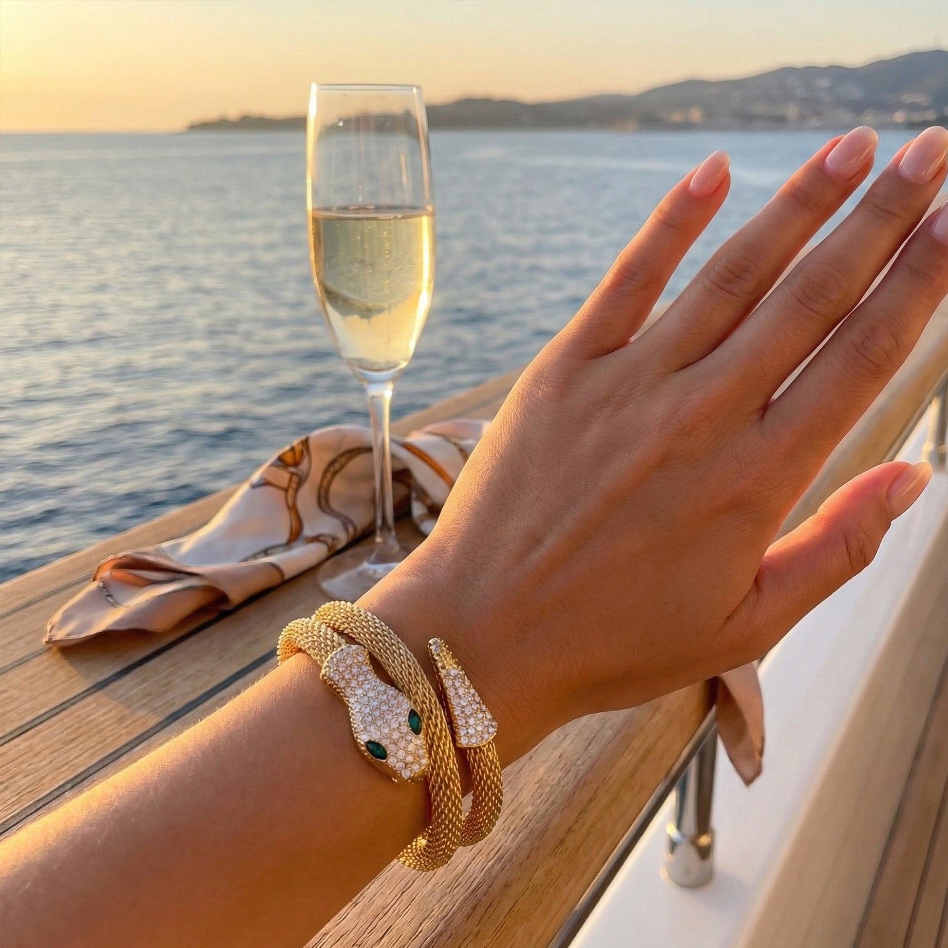 Woman wearing gold serpent mesh cuff on yacht background, styled with luxury resort wear.