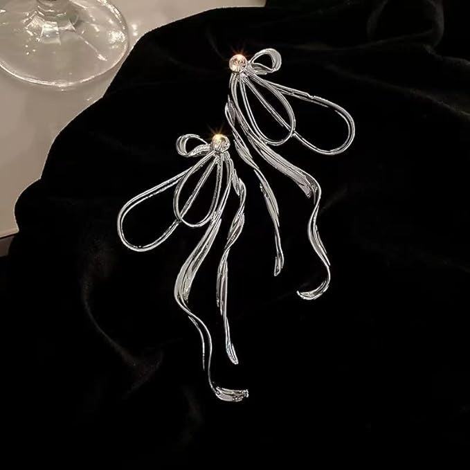 Silver bow earrings laid on black velvet, glowing under warm lighting