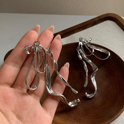 Close-up of exaggerated silver bow earrings with fluid, sculptural design on hand