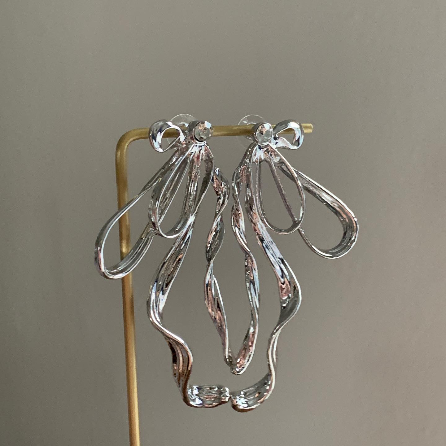 Earrings hung on a gold stand showcasing curved silhouette and polished finish