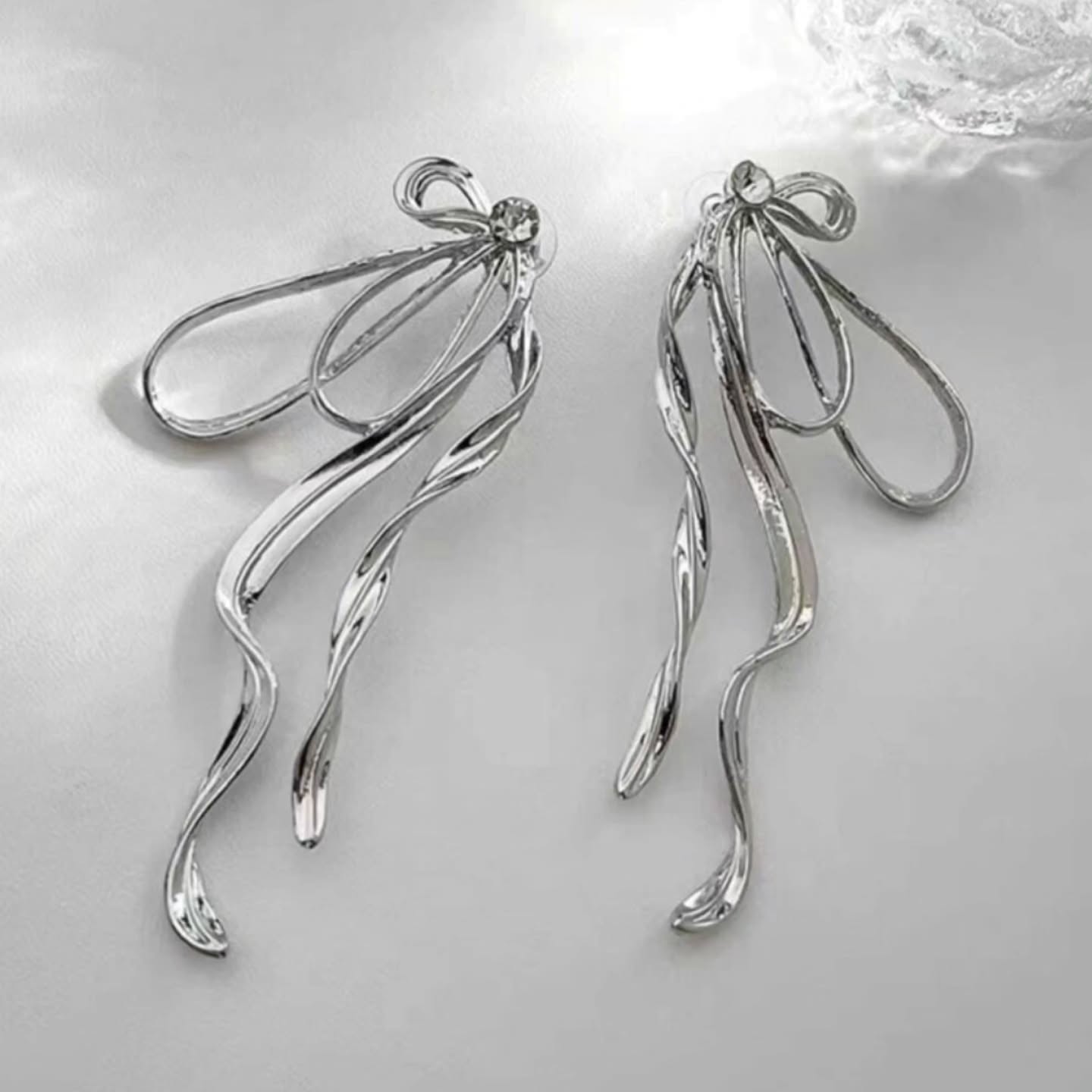 Glamorous silver bow earrings under soft light, highlighting reflective surface