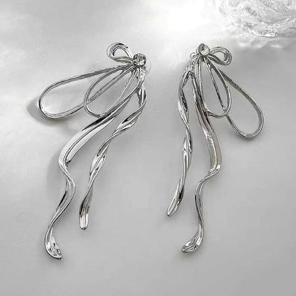 Glamorous silver bow earrings under soft light, highlighting reflective surface