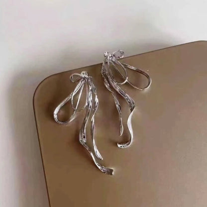 Silver bow earrings displayed on a brown surface with a modern minimal look