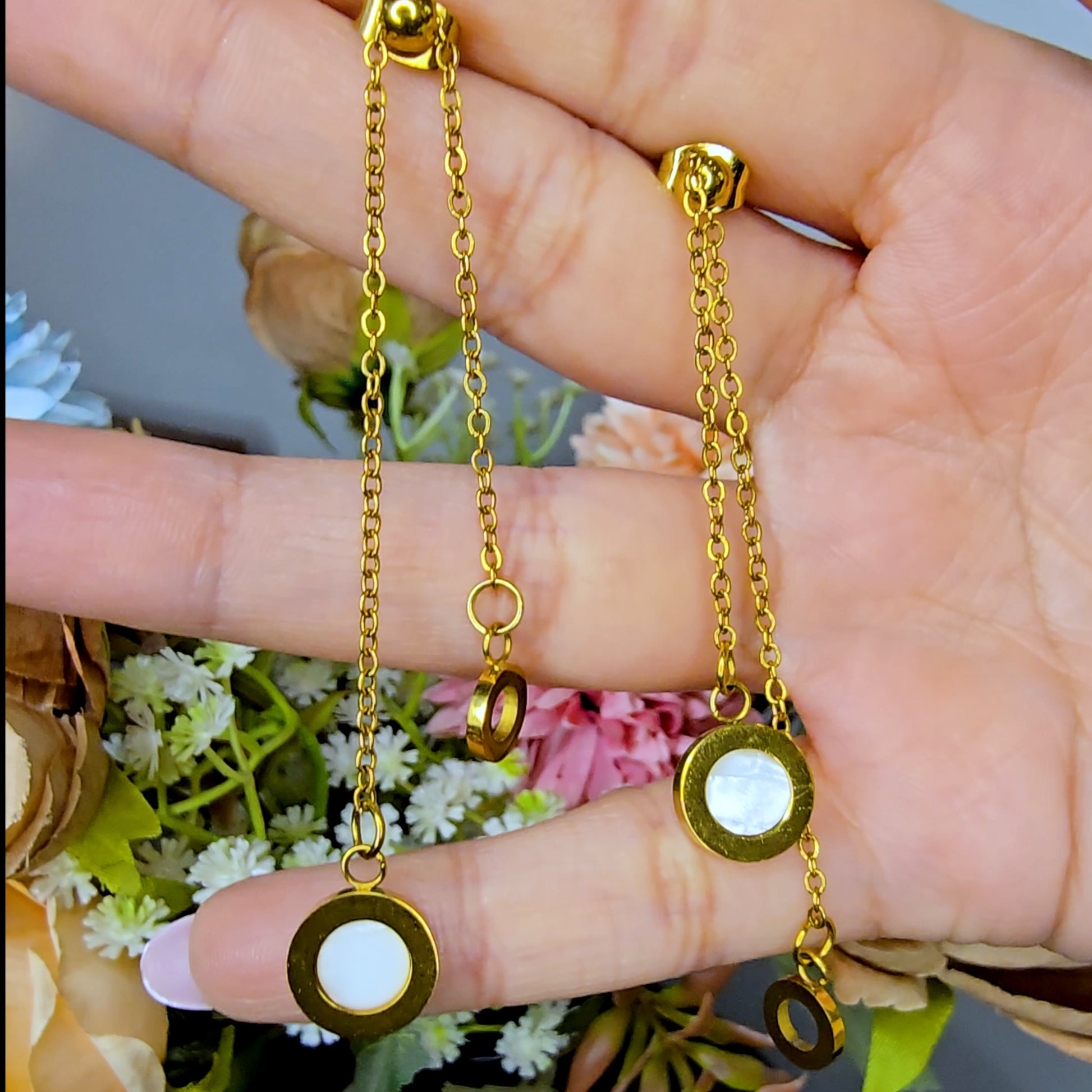 Hand holding long gold Slide Drop earrings to show the delicate chain lengths and reflective circular charms.