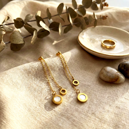 Aesthetic photography of gold Slide Drop earrings on beige linen cloth next to a gold ring and eucalyptus.