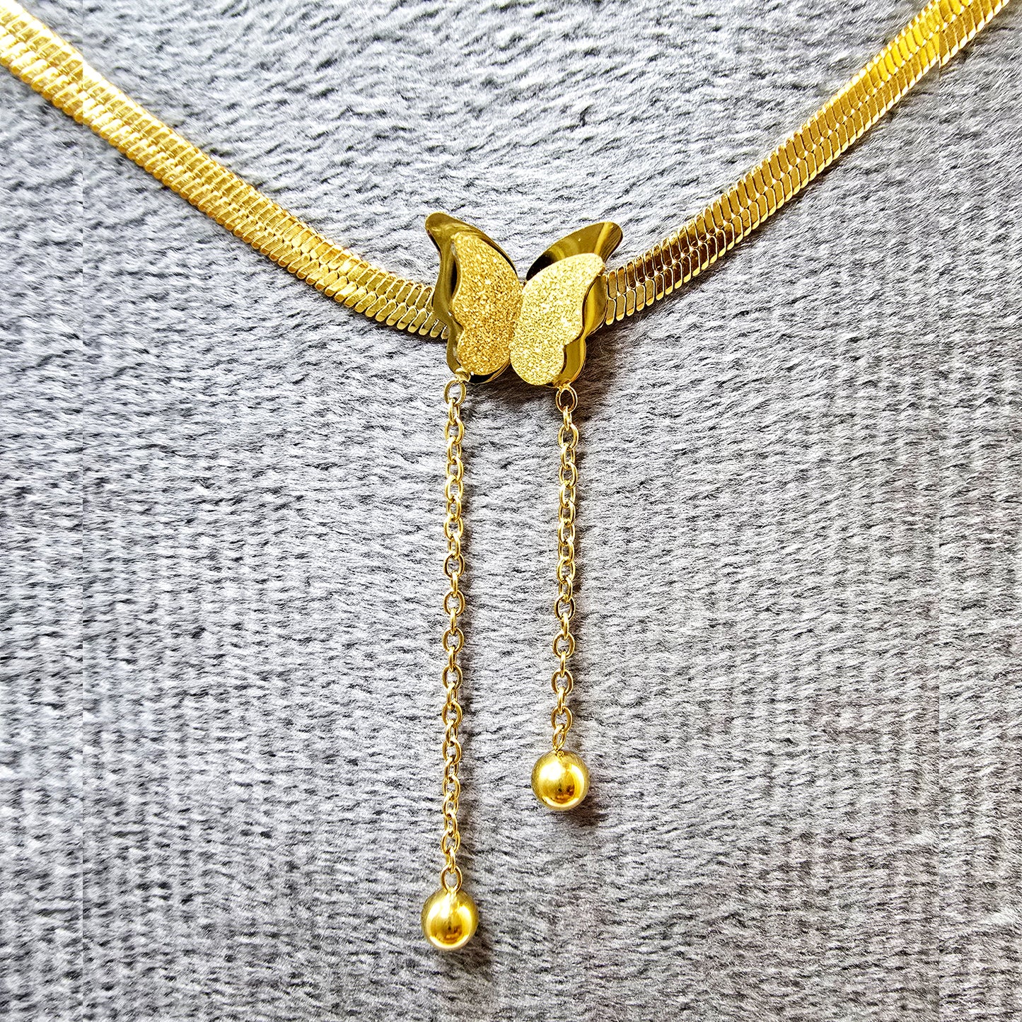 Close-up of butterfly pendant with textured wings and polished gold snake chain.