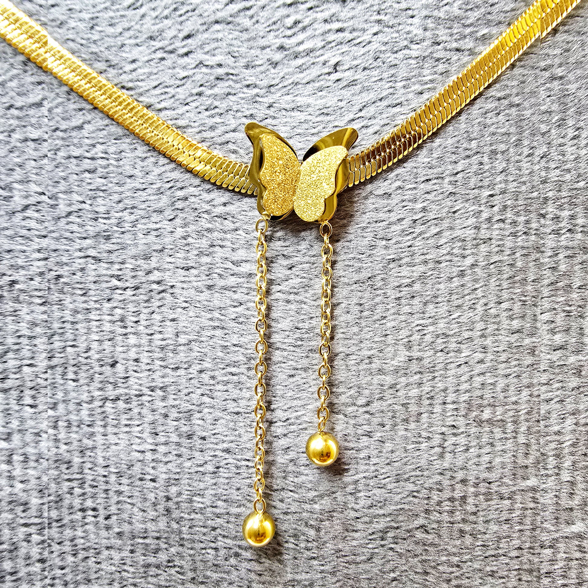 Close-up of butterfly pendant with textured wings and polished gold snake chain.