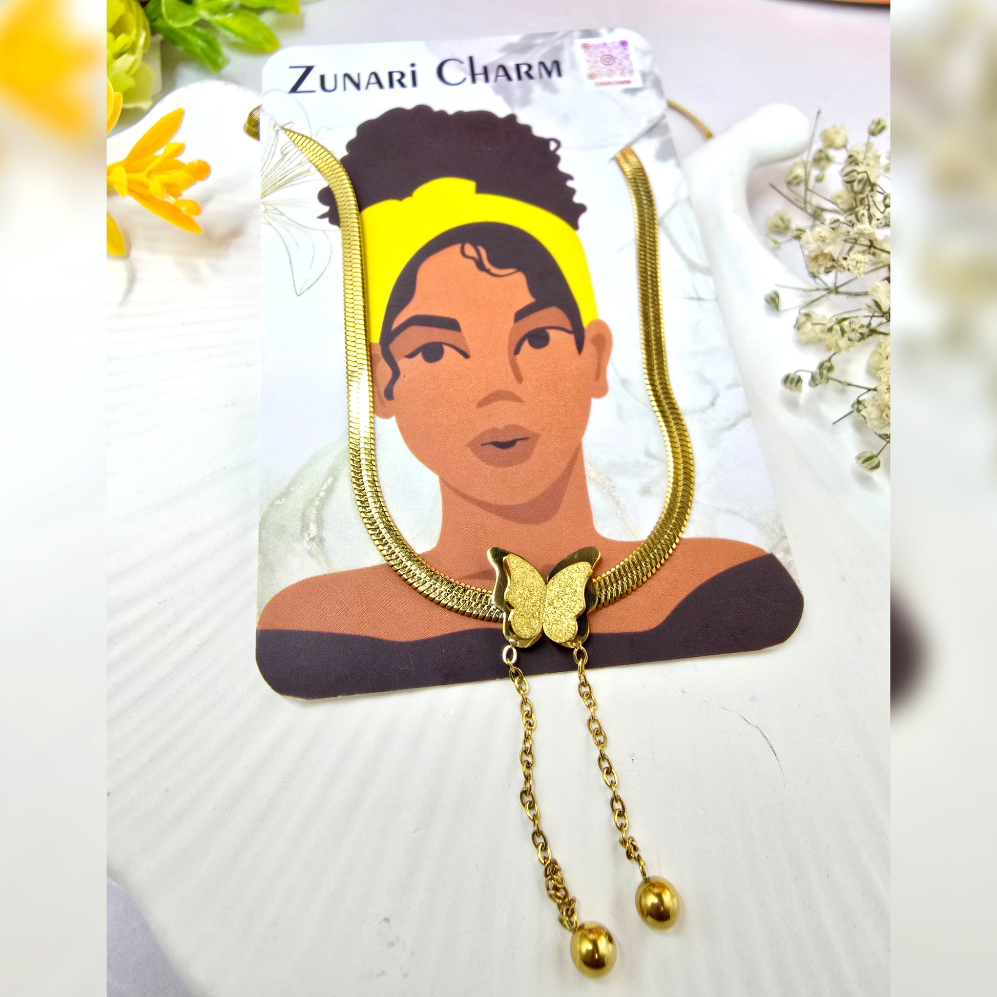 Necklace displayed on Zunari Charm packaging card – gold butterfly centerpiece with ball chain drops.