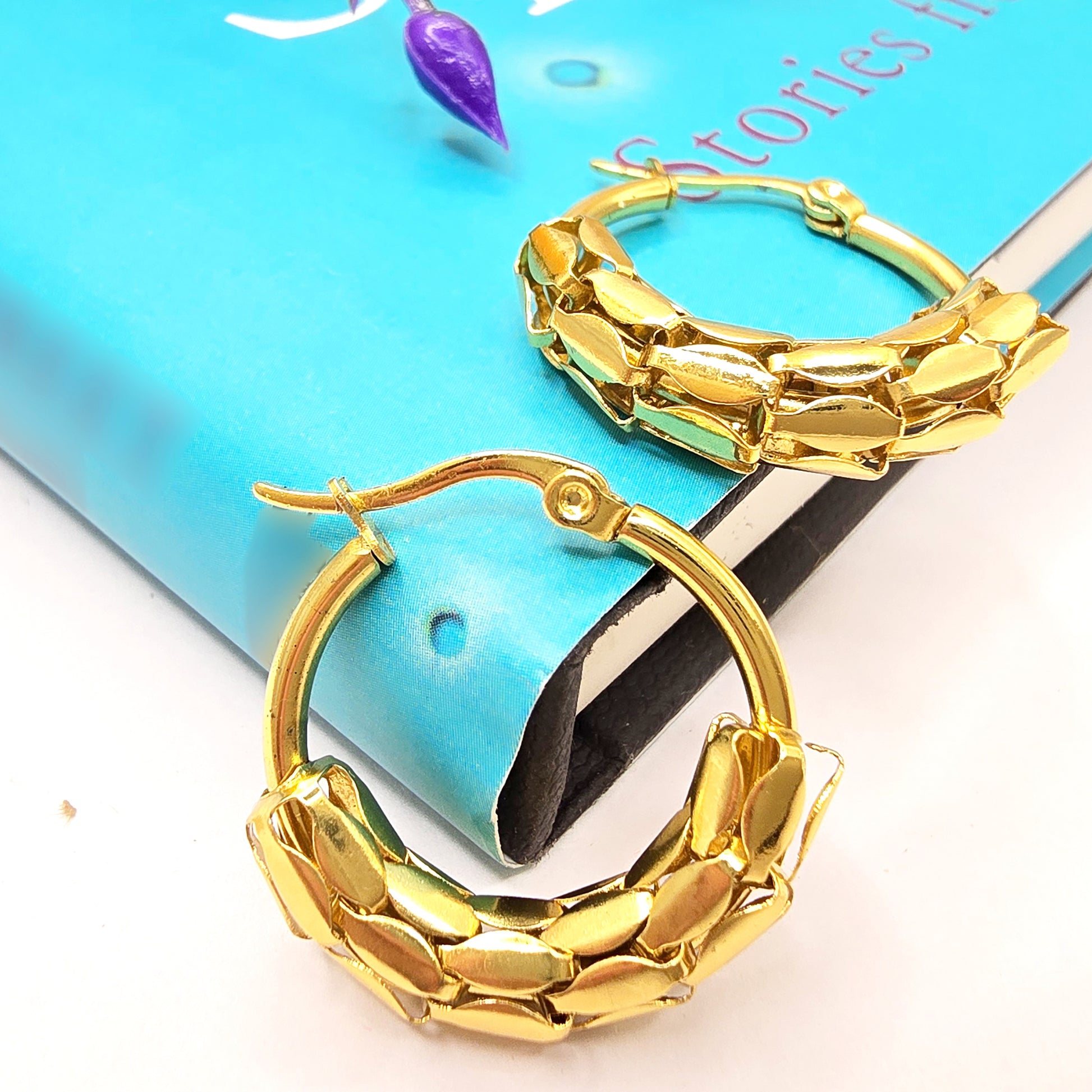 Snake Scale Earrings – gold textured hoops styled on a book